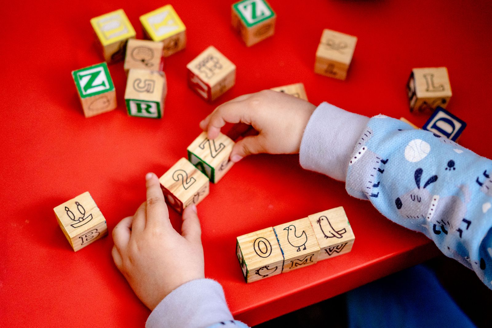 A child playing with wooden alphabet blocks alongside an adult